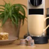 A coffee machine with a mug, coffee capsules, and a piece of cake. Produktbild-Vorschau