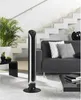A tall black and silver tower fan stands on a white rug in a modern living room with a gray sofa and stairs in the background. Produktbild-Vorschau