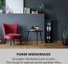 A wine cooler is shown in a stylish living room setting next to a red chair and a small table. Podgląd zdjęcia produktu