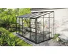 A greenhouse attached to a brick house, with plants and gardening tools around it. Produktbild-Vorschau