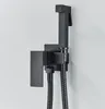 A black bidet sprayer and holder mounted on a light gray wall. Náhľad obrázku produktu