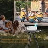 A family is watching a movie projected outdoors on a screen, with a projector set up on a tripod. Produktbild-Vorschau
