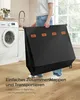 A person is holding a black laundry basket in a laundry room next to a washing machine. Produktbild-Vorschau