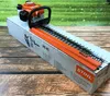 A Stihl hedge trimmer is placed on its box, with a blurred green background. Produktbild-Vorschau