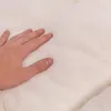 A hand is pressing into a soft, white, fluffy material, likely a dog bed. Produktbild-Vorschau