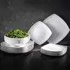 A set of white square plates and bowls filled with green salad, arranged on a dark surface against a black background. Náhľad obrázku produktu