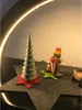 Christmas decorations including a tree and Santa Claus figures on a dark surface with a curved light. Produktbild-Vorschau