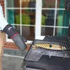 A person wearing a grilling glove is holding a fish on a grill. Produktbild-Vorschau