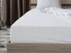 A white fitted sheet is shown on a bed with a wooden frame. Náhľad obrázku produktu