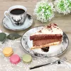 A coffee cup, saucer, slice of cake, and macarons are arranged on a wooden table with a lace tablecloth. Voir les images du produit