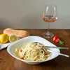 A table setting with pasta, bread, lemons, tomatoes, basil, and a glass of rosé wine. Voir les images du produit