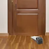 A doorstop alarm is placed on a wooden floor in front of a wooden door. Produktbild-Vorschau