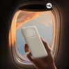 A hand holding a white power bank in front of an airplane window with a sunset view. Produktbild-Vorschau