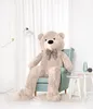 A large teddy bear sitting in a chair in a room with a lamp and side tables. Náhľad obrázku produktu