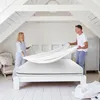A couple is making a bed in a bright, airy room with white wooden beams on the ceiling. Anteprima dell’immagine prodotto