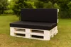 A white pallet sofa with black cushions sits on green grass in a garden setting. Produktbild-Vorschau