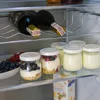 The image shows a shelf in a refrigerator with two bottles of wine and several jars of yogurt with fruit and granola. Náhled obrázku produktu