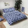 A bedroom scene with a bed dressed in blue and white patterned bedding, a large potted plant, and framed artwork. Produktbild-Vorschau