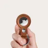 A hand holds a brown leather case for an Apple AirTag, with a silver snap and keyring. Produktbild-Vorschau
