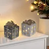 Two illuminated gift boxes are displayed on a white surface, with a blurred Christmas tree and lights in the background. Náhľad obrázku produktu