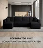 A modern living room with a black sectional sofa and a kitchen in the background. Produktbild-Vorschau
