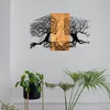 A metal wall art piece depicting two tree-like faces merging in the center, mounted on a wall above two potted plants. Produktbild-Vorschau