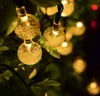 Close-up of solar-powered string lights with round, textured bulbs, nestled among green leaves. Voir les images du produit