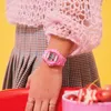 A close-up shot of a person's arm wearing a pink digital watch, with a pink knitted sweater and a plaid skirt visible. Produktbild-Vorschau