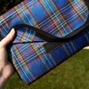 A hand holding a blue plaid picnic mat outdoors. Produktbild-Vorschau