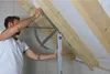 A man is using a measuring tool to check the angle of wooden beams in an attic. Anteprima dell’immagine prodotto