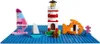 A Lego construction of a lighthouse, a sailboat, a fish, and a coral on a blue base plate representing water. Produktbild-Vorschau