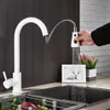 A white kitchen faucet with a pull-out spray is shown in use, with water spraying into a sink. A framed picture and a potted plant are visible in the background. Náhľad obrázku produktu