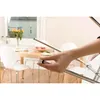 A hand is holding a small white and brown object, possibly a furniture protector, in front of a dining table with chairs and flowers. Anteprima dell’immagine prodotto