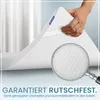 A hand holding up a corner of a white mattress topper, with a magnifying glass showing the textured underside. Produktbild-Vorschau