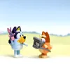 Two Bluey figurines are standing in a field with a blue sky. Voir les images du produit