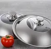 Two stainless steel pot lids with glass inserts and handles, along with a single red tomato, are placed on a gray surface. Produktbild-Vorschau