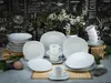 A collection of white porcelain dinnerware, including plates and cups, arranged on a table with a chalkboard-style background featuring various text and illustrations. Produktbild-Vorschau
