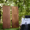Two tall, rectangular metal screens with a rust patina stand in a grassy area with trees in the background. A wooden chair with a dark furry blanket and a pillow with a deer image is placed to the right of the screens. Náhľad obrázku produktu