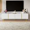 A modern white TV stand with gold accents and legs, placed in a living room setting with a large black TV above it and a patterned rug in front. Anteprima dell’immagine prodotto