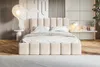 A modern bedroom with a plush beige bed as the centerpiece, styled with pillows and a throw blanket. The room features textured wall art, a unique pendant lamp, and a wooden floor. Náhled obrázku produktu