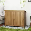 A wooden garden cabinet is placed on a bed of pebbles next to a grassy area and a wall with hanging plants. Produktbild-Vorschau