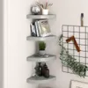 Four gray corner shelves are mounted on a light gray wall, displaying various decorative items and books. Produktbild-Vorschau