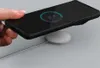 A hand holding a smartphone with a charging indicator on the screen, placed on a wireless charger. Produktbild-Vorschau