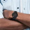 A close-up shot of a man's arm wearing a black Tommy Hilfiger watch. Produktbild-Vorschau