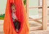A young boy is happily sitting in an orange hanging chair, which is part of a wooden play structure. Produktbild-Vorschau