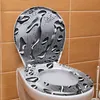 A toilet seat and lid with a water droplet design, set against a tiled wall. Produktbild-Vorschau