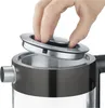 A hand is shown opening the lid of a black and silver kettle. Podgląd zdjęcia produktu