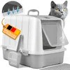 A British Shorthair cat peeks over a closed litter box with a scoop and a German company tag. Produktbild-Vorschau