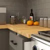 A kitchen countertop with various items, including a countertop, cabinets, a microwave, jars, oranges, and a wine bottle. Produktbild-Vorschau