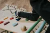 A child's legs and feet are visible as they climb on a wooden structure with colorful grips. The scene is indoors, with a rug and wooden floor visible in the background. Produktbild-Vorschau